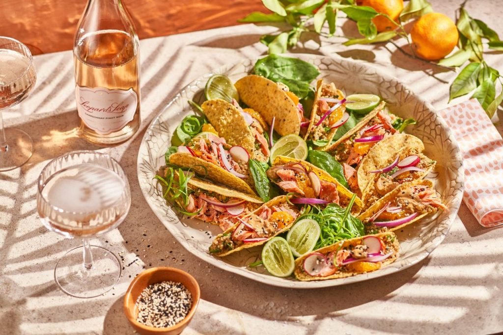 A large speckled platter of salmon tacos with radish, lime and citrus, beside a bottle of Leopard's Leap Sparkling Chardonnay Pinot Noir in dappled sunlight